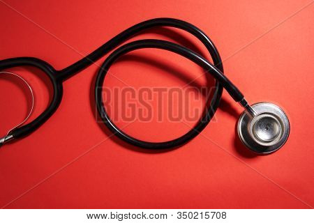 black stethoscope on a red background top view with copy space.