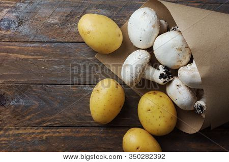 Bunch Of Freshly Picked White Button Mushrooms Potatoes In Brown Paper Bag On Rustic Wood Table. Pla