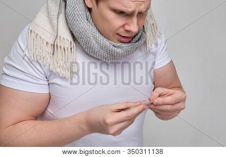 A Man In A White T-shirt With A Scarf Looks At The Thermometer In Surprise. The Concept Of Lowered B