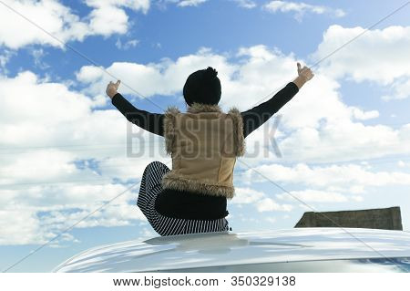 Woman On The Roof Of The Car With Her Hands Up And Blue Sky