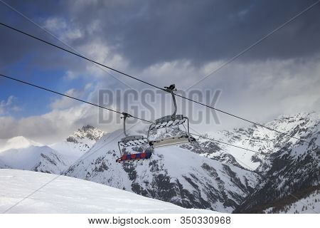 Sunlit Chair Lift, Snowy Ski Slope, High Winter Mountains And Dark Cloudy Sky. Ski Area Mottolino Fu