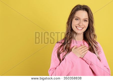 Beautiful Grateful Woman With Hands On Chest Against Yellow Background. Space For Text