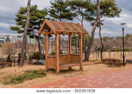 Wooden Covered Park Bench In Public Park Under Cloudy Sky.