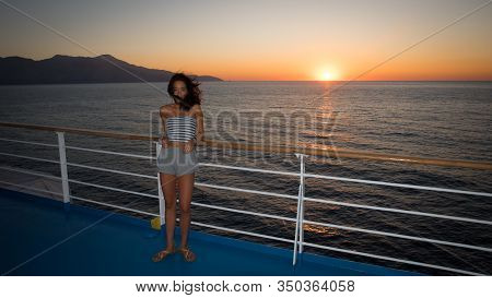 Asian Teen In Tube Top Standing On Deck Of Ferry Looking Away From Sunset On Ferry To Greece
