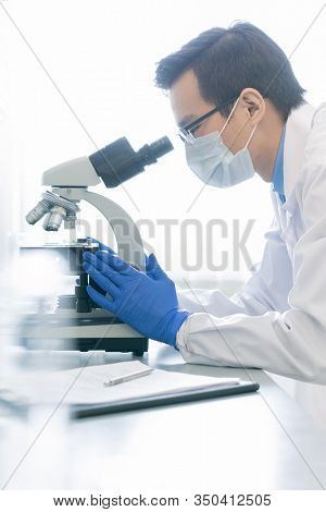 Vertical side view portrait of young male pharmacologist examining specimen chemical reaction using microscope in modern laboratory