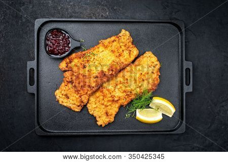 Traditional deep fried Wiener schnitzel from veal topside with cranberry jam and lemon slices offered as top view on a black modern design tray  