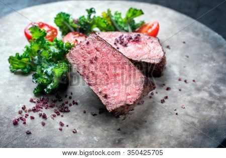 Barbecue dry aged wagyu roast beef natural sliced offered with rapini and tomatos as closeup on a modern design plate 
