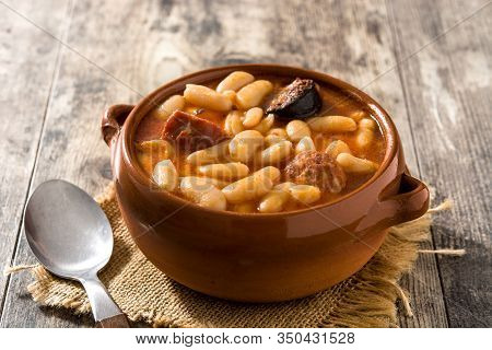 Typical Spanish Fabada Asturiana In Crockpot On Wooden Table