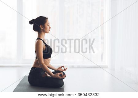 Ardha Padmasana Exercise. Side View Of Fit Girl Meditating Sitting In Lotus Pose On Gray Yoga Mat By
