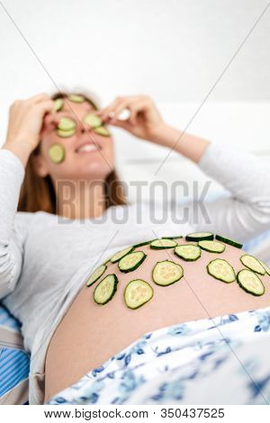 A Caucasian Pregnant Woman Lies On Her Bed And Puts Slices Of Cucumbers On Her Face And Tummy, Spa-d
