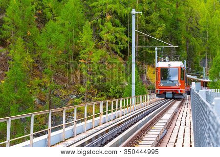 Zermatt, Switzerland Arriving Gornergrat Red Tourist Train Front View On The Bridge In Swiss Alps