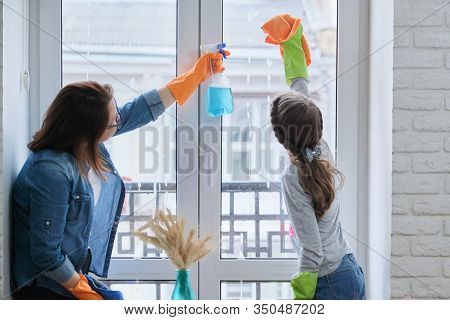 Mother And Daughter Child In Rubber Gloves With Detergent And Rag Washing Windows Together. Girl Hel