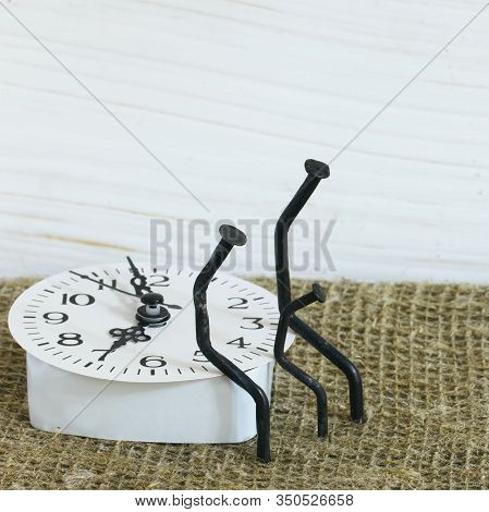 Figurines Of Man Made From Carpentry Nails. They Are Sitting On The Watch Dial, Next To Each Other.
