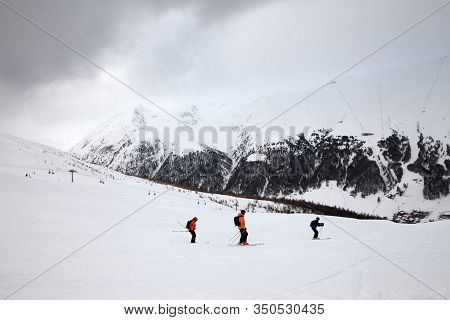 Off-piste Snowy Ski Slope With Skiers In High Mountains And Cloudy Sky At Winter Grey Day. Ski Area 