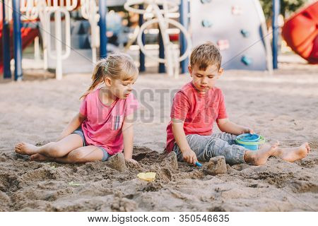 Two Caucasian Children Sitting In Sandbox Playing With Beach Toys. Little Girl And Boy Friends Havin