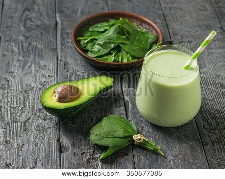 A Bowl Of Spinach Leaves, Half An Avocado, And A Glass Of Smoothies On A Black Wooden Table. Fitness