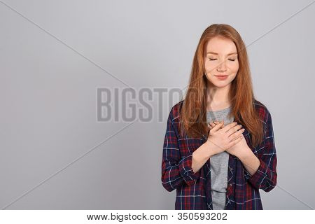 Beautiful Grateful Woman With Hands On Chest Against Light Grey Background. Space For Text