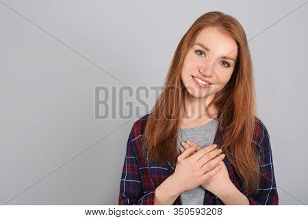 Beautiful Grateful Woman With Hands On Chest Against Light Grey Background. Space For Text