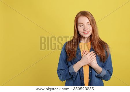 Beautiful Grateful Woman With Hands On Chest Against Yellow Background. Space For Text