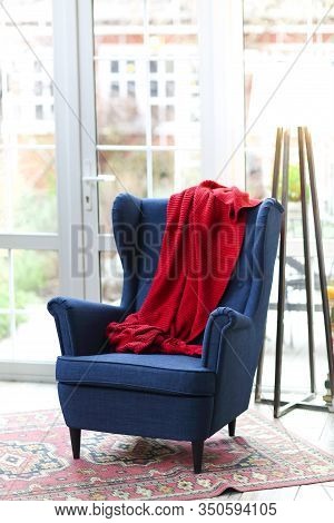Stylish Wing Chair In Majestic Indigo Color With Bright Red Plaid On Back Placed On Carpet Against B