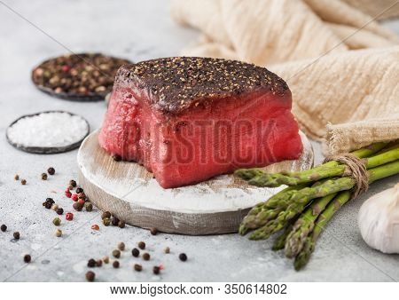Slice Of Raw Beef Topside Joint With Salt And Pepper On Round Chopping Board With Asparagus Tips And