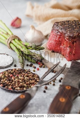 Slice Of Raw Beef Topside Joint With Salt And Pepper On Round Chopping Board With Fork And Knife, As