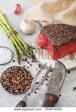 Slice Of Raw Beef Topside Joint With Salt And Pepper On Round Chopping Board With Fork And Knife, As