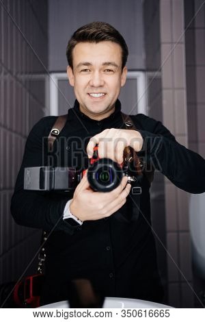 Photographer In Black Clothes Taking A Selfie With The Camera In The Mirror And Smiling