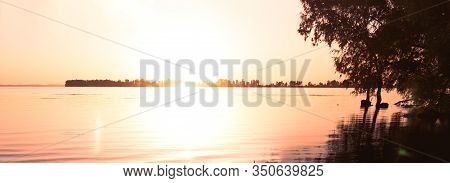 Panoramic Shot Of Sinrise Above River And Beach With Trees