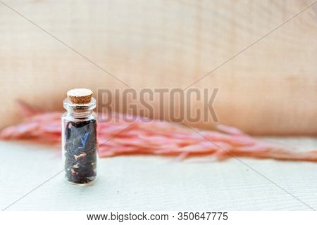 Small Old Vintage Glass Bottle With Cork With Floral Tea And Blue And Pink Petals On Wooden Backgrou
