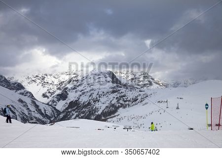 Snowy Ski Slope With Skier And Snowboarder In High Mountains And Cloudy Sunlit Sky At Winter Gray Da