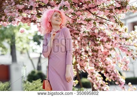 Happy Young Woman With Curly Pink Hair And Sunglasses Near The Blossoming Spring Tree.