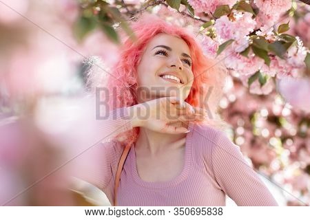 Close-up Portrait Of Bright Young Woman With Curly Pink Hair And Sunglasses Near The Blossoming Spri