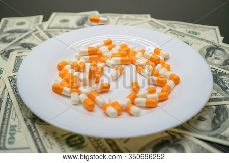White Plate With Orange-and-white Tablets On The Table With Dollar Bills. Photos Of Falling Tablets 