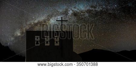 Cross On Church Over Clear Night Sky And Bright Milky Way . Six Bells Of Different Sizes On The Top.