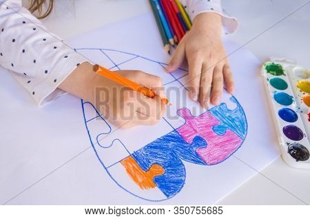 A Child Is Drawing Colorful Heart With Jigsaw Puzzle On White Background As A Symbol Of Autism, With