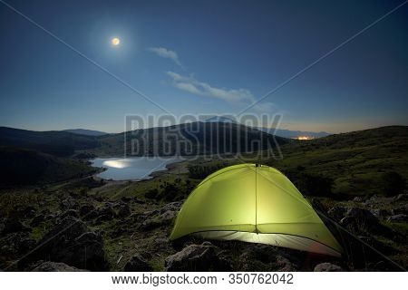illuminated tent and night full moon reflection on lake of Nebrodi Park, Sicily