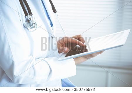 Woman Doctor Using White Tablet Computer While Sitting At Chair In Hospital, Close-up