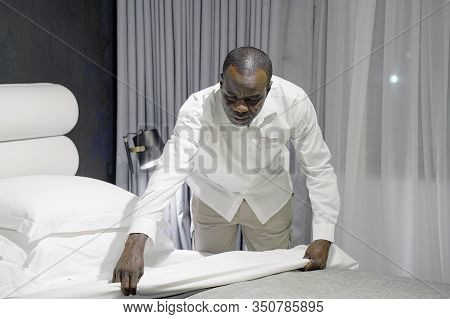 Elderly Maid Making Bed In Hotel Room. Staff Maid Making Bed. African Housekeeper Man Making Bed.