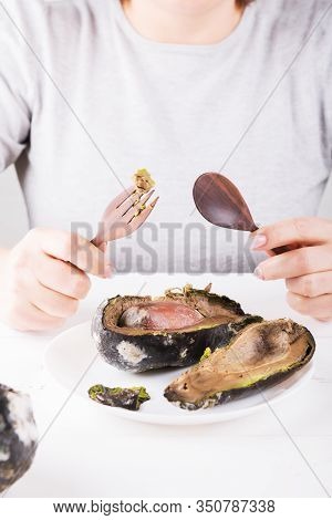 A Faceless Man Sits At A Table, With A Knife And A Fork In His Hands In Front Of A Plate Of Rotten A