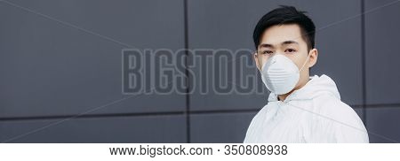 Panoramic Shot Of Asian Epidemiologist In Hazmat Suit And Respirator Mask Looking At Camera While St