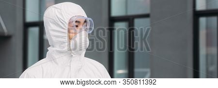 Panoramic Shot Of Asian Epidemiologist In Hazmat Suit And Respirator Mask Looking Away While Standin