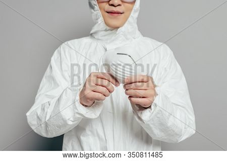 Cropped View Of Epidemiologist In Hazmat Suit Holding Respirator Mask On Grey Background