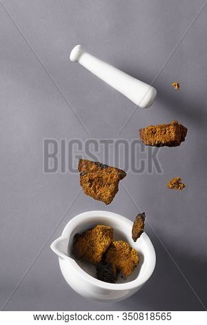 Dry Wild Chaga Mushroom Pieces, White Pestle And Meortar Falling On The Grey Background, Inonotus Ob