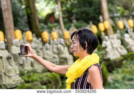mature Asian woman take a picture at a garden with arhat stone statues
