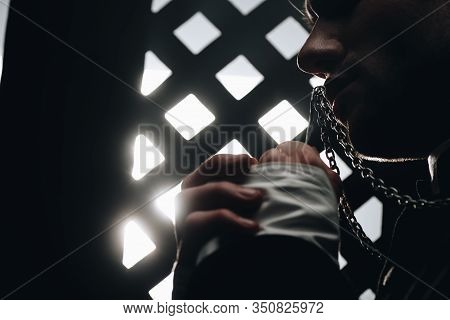 Cropped View Of Catholic Priest Kissing Cross On His Necklace Near Confessional Grille In Dark With 