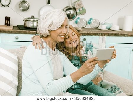 Senior White Haired Cassually Dressed Grandmother Taking Photo With Her Granddaughter In Blue Jeans 