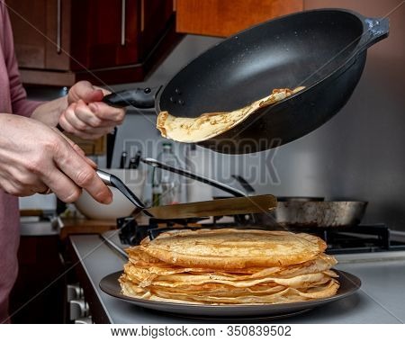 Human Hands Holding A Spatula And A Frying Pan Spread Hot Pancake On The Dish From Which Steam Comes