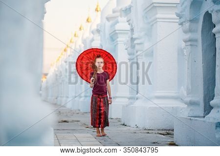 Young girl with traditional burmese umbrella at beautiful white Kuthodaw Pagoda in Mandalay Myanmar