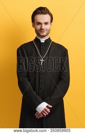 Young Catholic Priest Smiling At Camera While Standing Isolated On Yellow